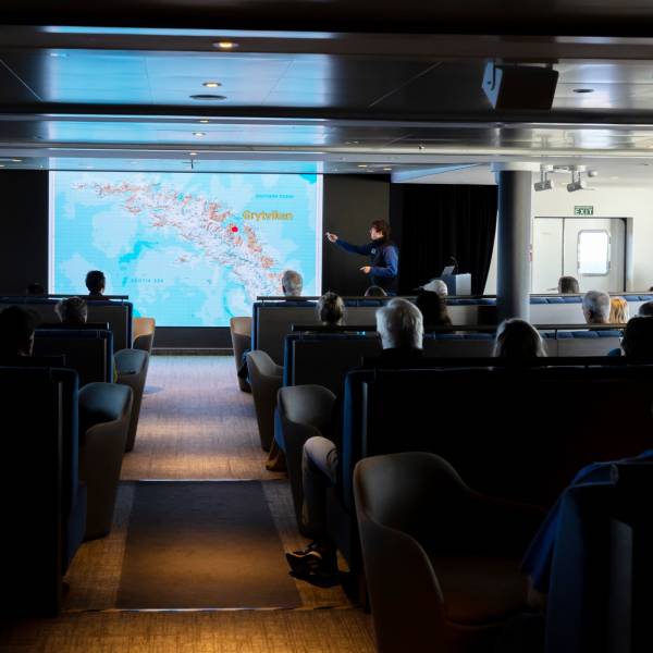 A presenter stands in front of a large screen displaying educational content about polar regions, engaging the audience with visual aids and maps