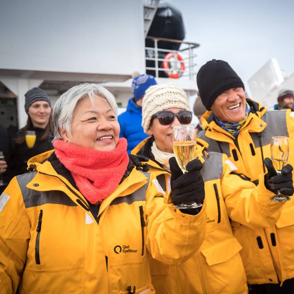 Guests celebrate crossing the Antarctic Circle with sparkling beverages and taking photos on the deck of the ship.