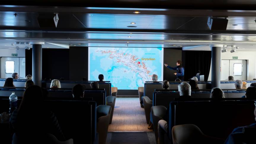 A presenter stands in front of a large screen displaying educational content about polar regions, engaging the audience with visual aids and maps