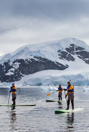 Four guests on their standup paddleboards paddle through calm waters in Antarctica.