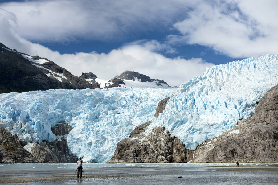 A photographer with a tripod stands in front of Capella Glacier at Santa Ines Island in the West Strait of Magellan.