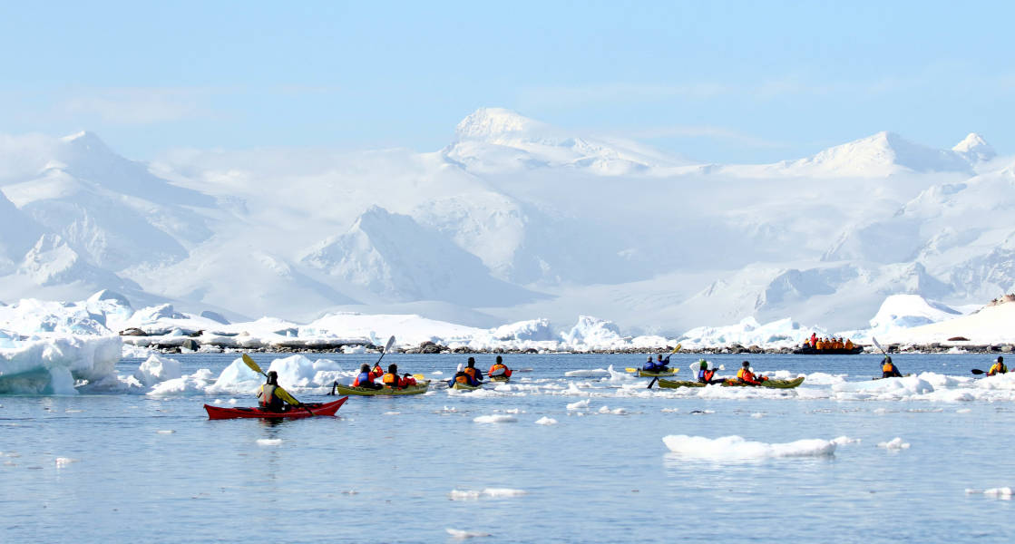 Guests kayaking through frigid waters in Antarctica. Two guides accompany the main group.