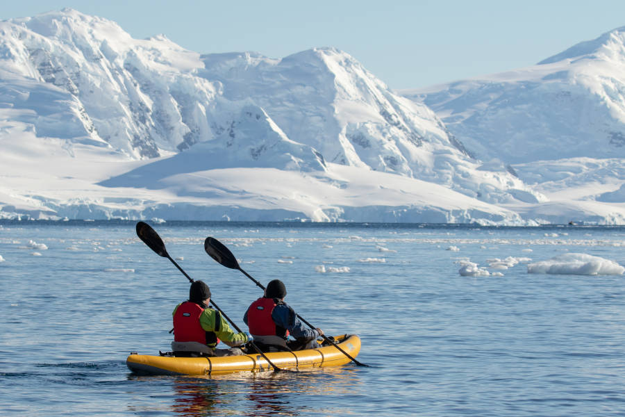 Two guests in dry suits paddle through Antarctic waters onboard our sit-on-top inflattable kayaks.