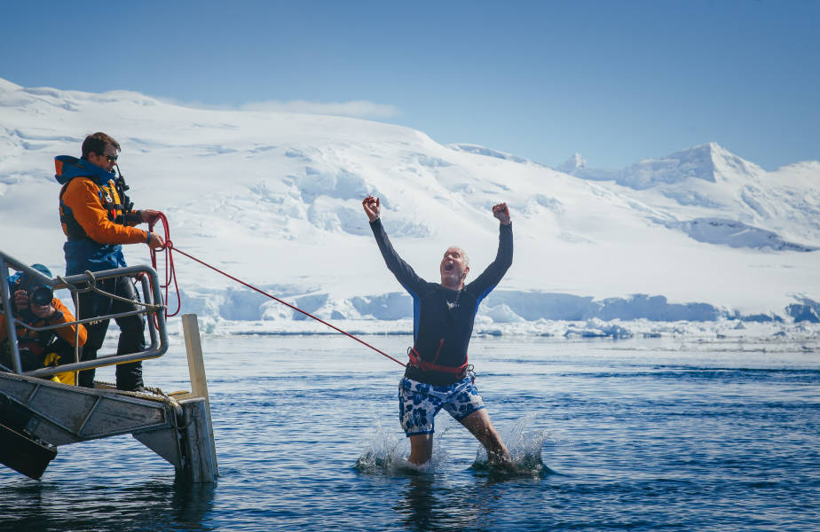A guest secured with a harness jumps into Antarctic waters from a gangway/platform on their vessel.