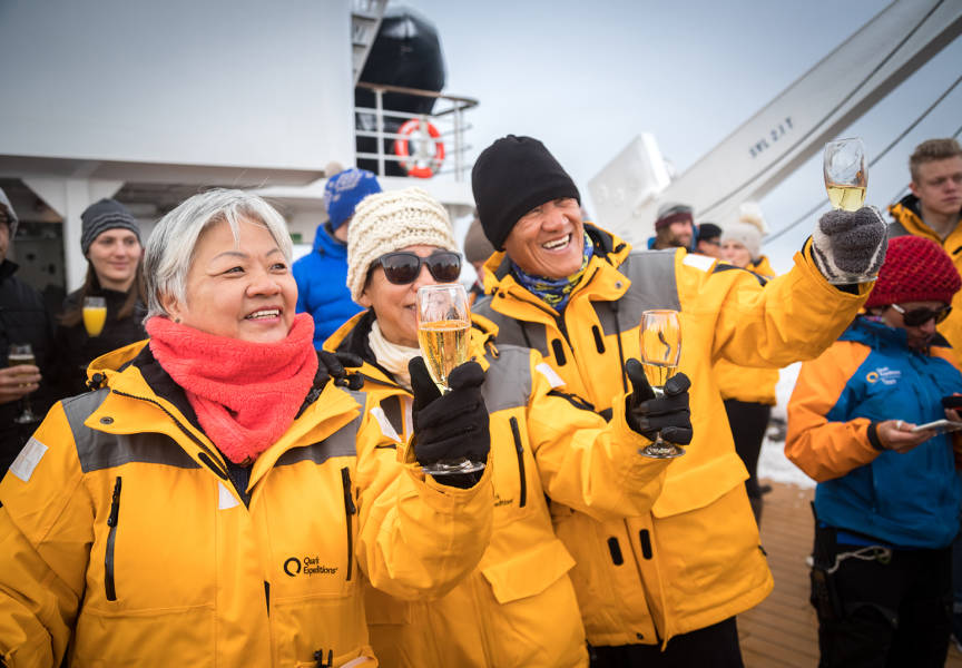 Guests celebrate crossing the Antarctic Circle with sparkling beverages and taking photos on the deck of the ship.