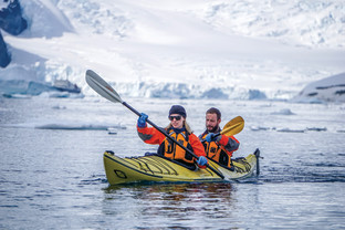 Two guests in their dry gear paddle a kayak in the frigid Antarctic waters during a sunny day.
