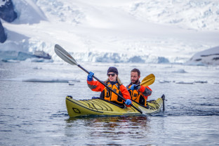 Two guests in their dry gear paddle a kayak in the frigid Antarctic waters during a sunny day.