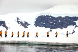 Guests in yellow parkas walk in a single file during a sea ice landing