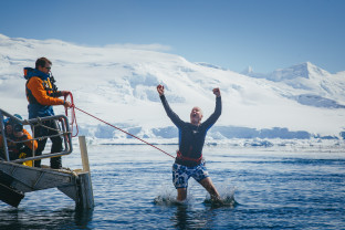 A guest secured with a harness jumps into Antarctic waters from a gangway/platform on their vessel.