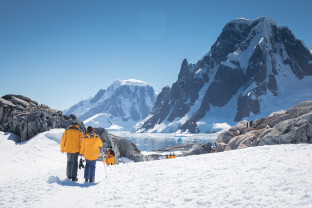 Guests in yellow parkas follow the marked trail at Petermann Island during a sunny day in the Antarctic Peninsula.
